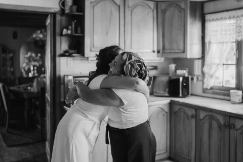 Dos mujeres abrazándose dentro de una cocina en una fotografía en blanco y negro.