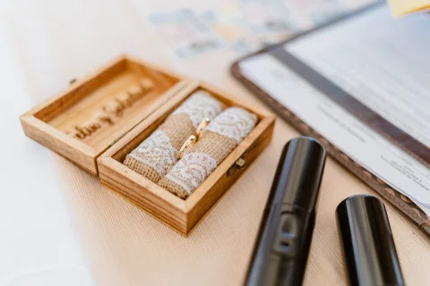 Dos anillos descansan dentro de una caja de madera junto a un documento y dos objetos negros.