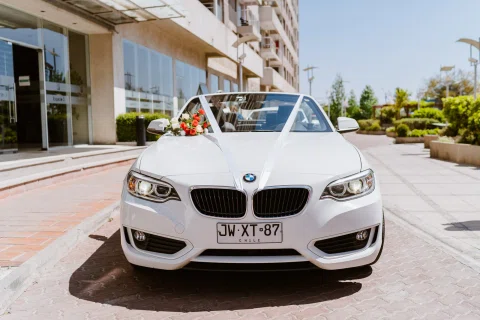 Automóvil blanco decorado con flores y una cinta estacionado frente a un edificio.