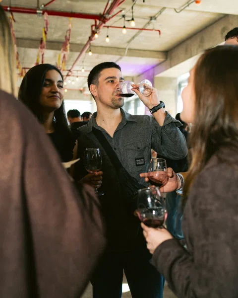Grupo de asistentes con copas de vino; un hombre bebe de su copa.