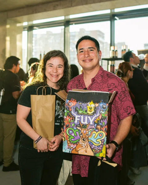 Dos personas posan con una bolsa de papel y una caja ilustrada.