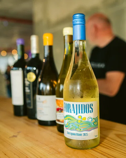 Botella de Sauvignon Blanc Forajidos en primer plano sobre una mesa de madera, con otras botellas al fondo.