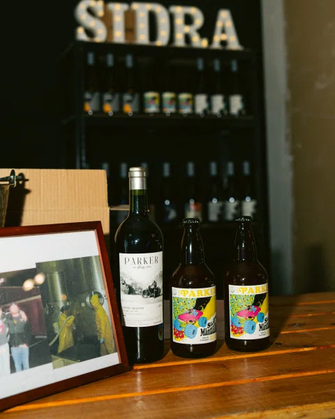 Botellas sobre una mesa de madera, con un letrero iluminado al fondo.