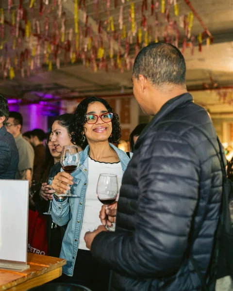 Dos personas conversan mientras sostienen copas con vino tinto.