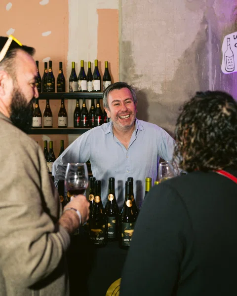 Tres personas conversan junto a una mesa con botellas y copas.