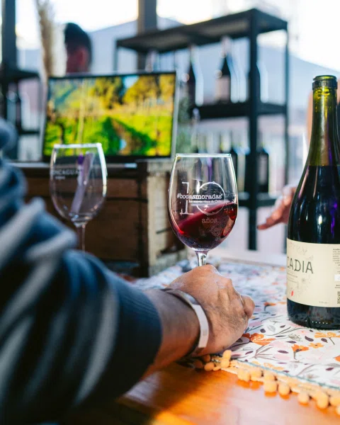 Copa con vino tinto sostenida sobre una mesa junto a una botella.