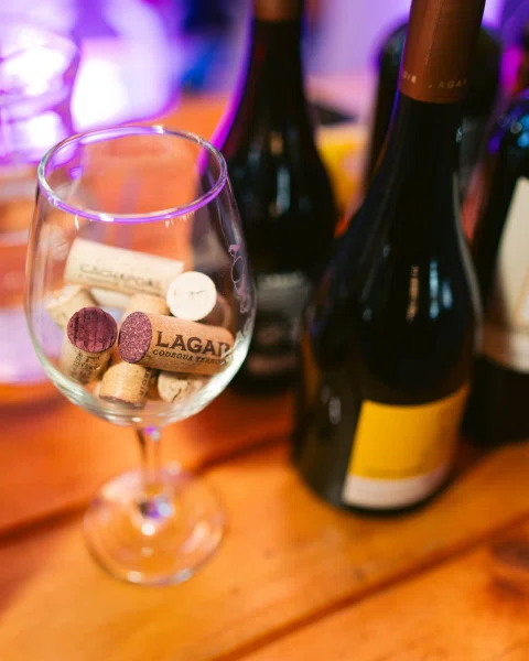 Copa con corchos y botellas sobre una mesa de madera iluminada en tonos violeta.