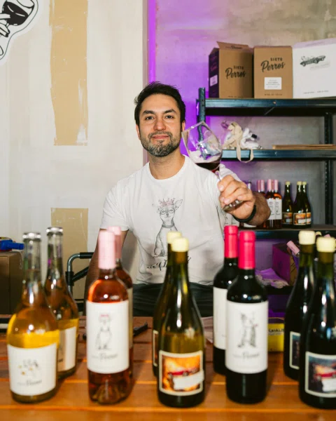 Hombre sostiene una copa de vino detrás de una mesa con botellas.