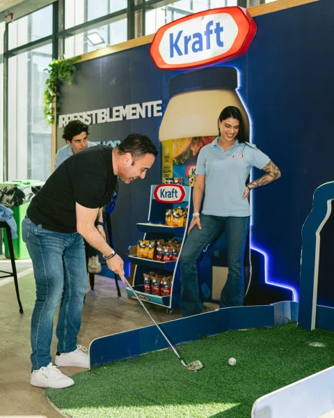 Hombre golpea una pelota en una instalación de minigolf frente a un panel de Kraft.