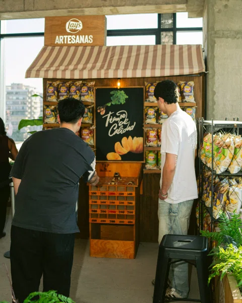 Dos personas participan en un juego frente a un puesto con letrero de Lay's Artesanas.