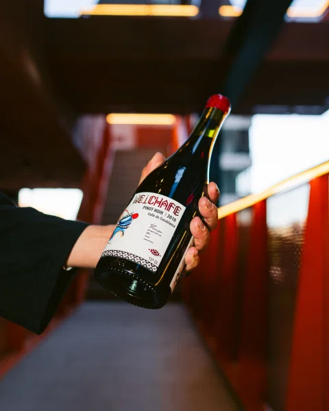 Mano sosteniendo una botella de vino Weichafe en un pasillo con paredes naranjas.