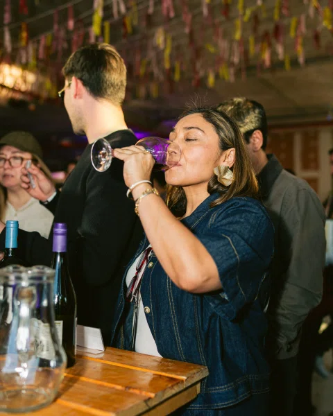 Mujer bebe de una copa de vino junto a una mesa con botellas.