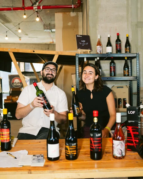 Dos personas muestran botellas detrás de una mesa con vinos LOF.