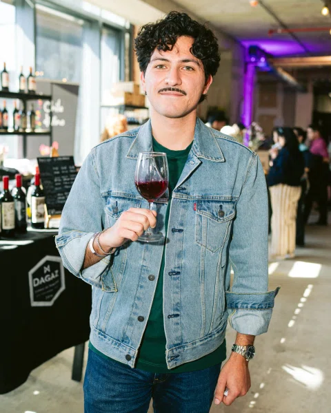 Hombre con chaqueta de mezclilla sosteniendo una copa de vino tinto.