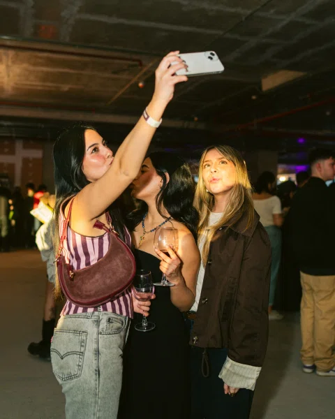 Tres mujeres se toman una selfie; dos de ellas sostienen copas.