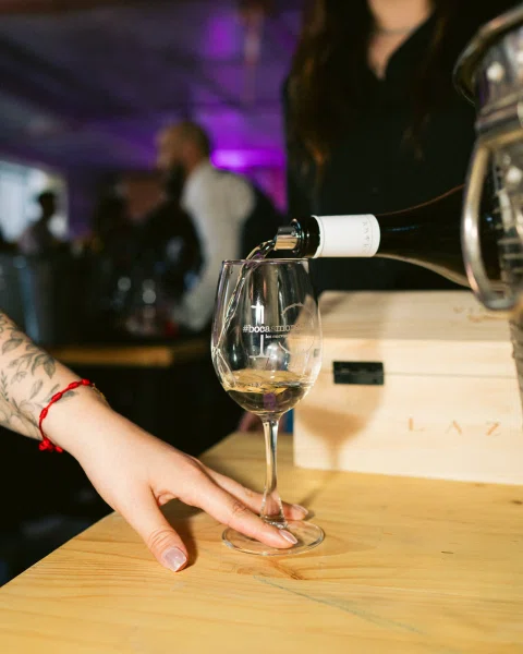 Una persona sirve vino blanco en una copa sobre una mesa de madera.