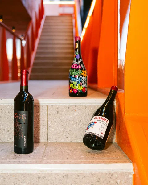 Tres botellas de vino dispuestas en distintos escalones junto a paredes naranjas.