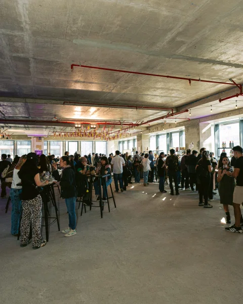 Vista amplia de asistentes reunidos en un espacio interior con mesas altas.