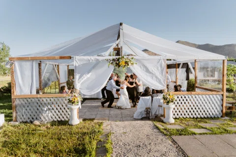 Carpa blanca instalada en un jardín, con decoración floral y varias personas en su interior.