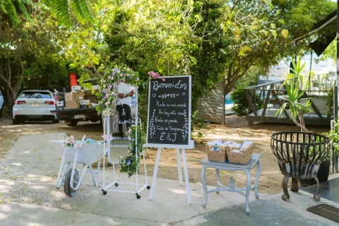Cartel de bienvenida y mobiliario decorativo instalados al aire libre entre árboles.
