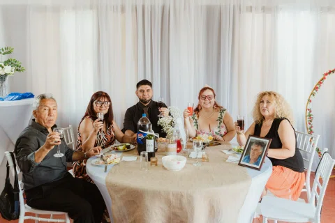 Cinco personas posan sentadas alrededor de una mesa con platos y bebidas.