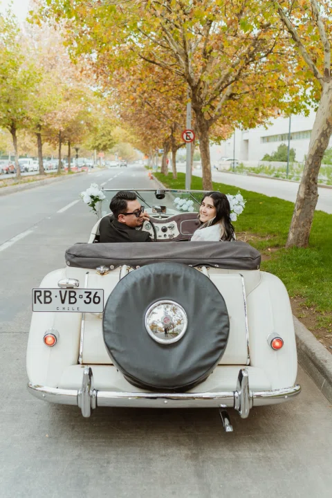 Vista trasera de un automóvil convertible blanco con dos personas sentadas en su interior.