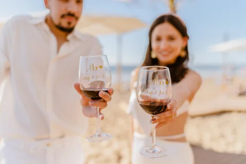 Dos copas de vino aparecen en primer plano con un hombre y una mujer desenfocados detrás.