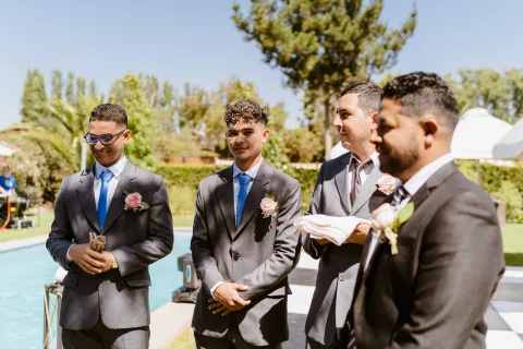 Cuatro hombres con traje permanecen reunidos junto a una piscina; uno sostiene una cuerda enrollada.