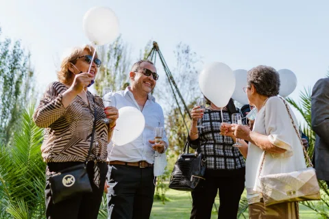 Cuatro personas sostienen globos blancos y copas durante la celebración al aire libre.