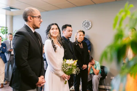 Cuatro personas permanecen de pie juntas; una mujer con vestido blanco sostiene un ramo.