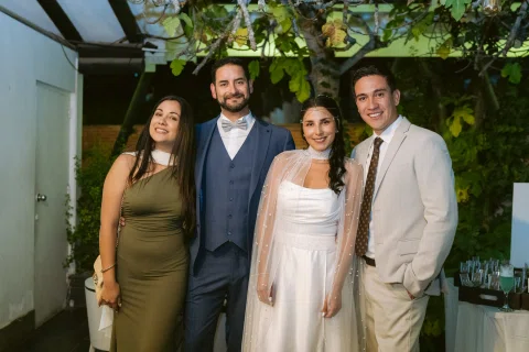 Cuatro personas posan juntas bajo luces nocturnas; una mujer viste blanco y uno de los hombres lleva traje azul.