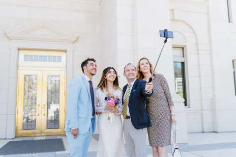 Cuatro personas posan juntas para una selfie en el exterior del edificio; una de ellas sostiene el teléfono en una vara.