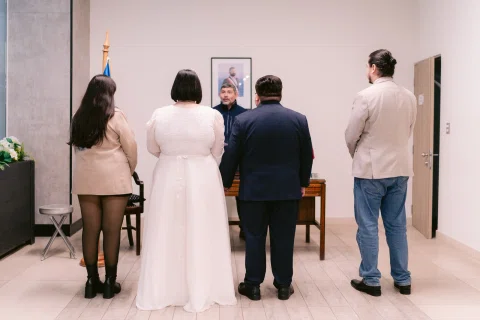 Cuatro personas vistas de espaldas permanecen frente a una mesa, con una bandera chilena a un costado.
