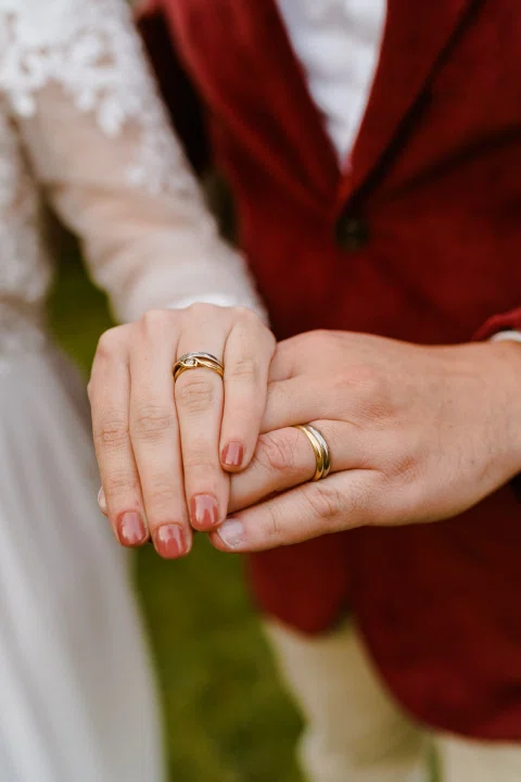 Detalle de dos manos con anillos superpuestas frente a una chaqueta roja.