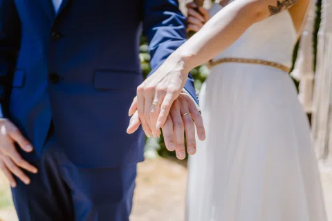 Detalle de dos manos con anillos junto a un vestido blanco.