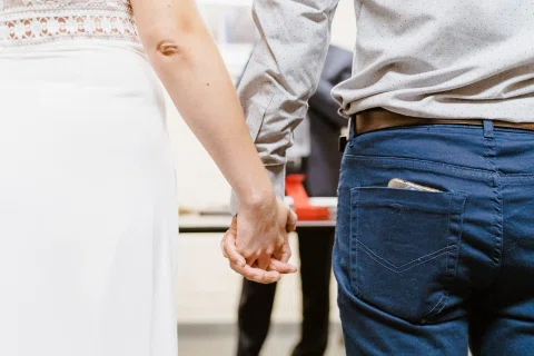 Detalle de dos manos entrelazadas, junto a una camisa celeste y un vestido blanco.