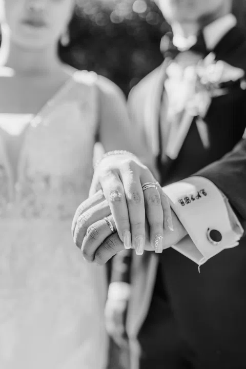 Detalle en blanco y negro de las manos superpuestas de un hombre y una mujer, con anillos visibles.