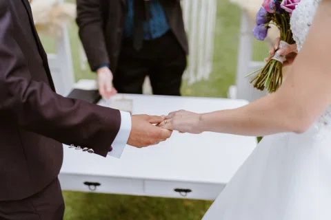 Detalle de las manos de un hombre y una mujer tomadas junto a una mesa blanca.