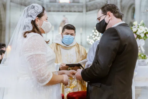 Detalle de una mujer con vestido blanco y un hombre con traje oscuro tomados de las manos frente al altar.