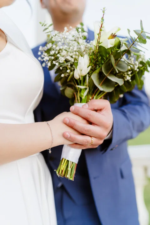 Detalle de un ramo de flores sostenido por una mujer con un hombre parcialmente visible detrás.