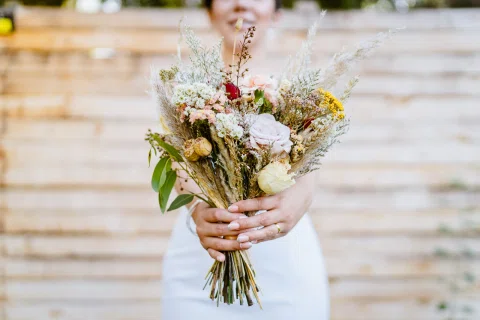 Detalle de un ramo de flores silvestres sostenido por una mujer con vestido blanco.