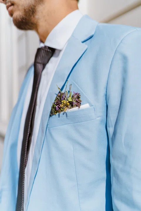 Detalle de la solapa de un traje celeste con una pequeña flor.