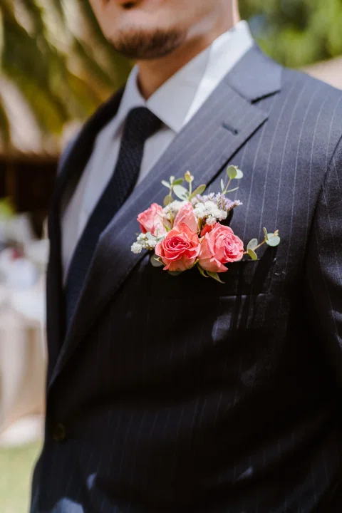 Detalle de la solapa de un traje oscuro con una flor rosada prendida.