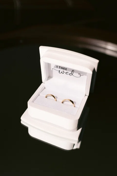 Dos anillos descansan dentro de una caja blanca abierta sobre fondo oscuro.