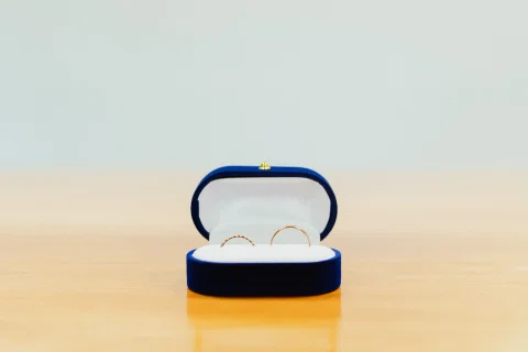 Dos anillos dentro de una pequeña caja azul abierta sobre una mesa.