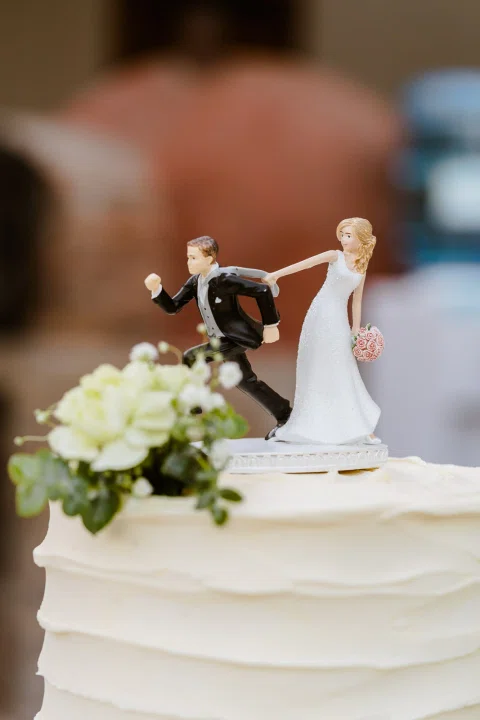 Dos figuras decorativas, una con traje oscuro y otra con vestido claro, aparecen sobre una torta blanca.