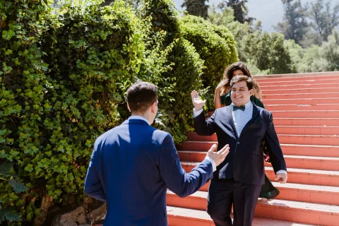 Dos hombres con traje se saludan junto a una escalera roja en un jardín.