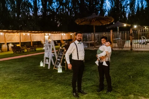 Dos hombres posan en el jardín; uno de ellos sostiene a un niño en brazos.