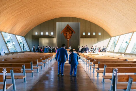 Dos hombres con traje caminan de espaldas por el pasillo central de una capilla.