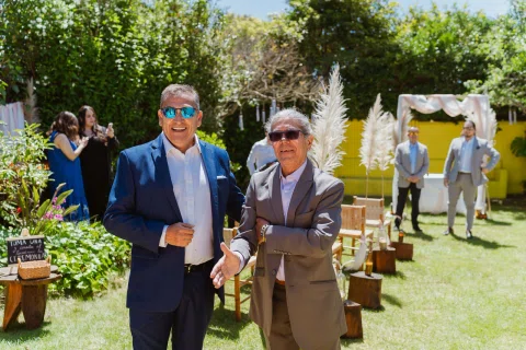 Dos hombres con traje permanecen en el jardín; uno viste azul y el otro gris.